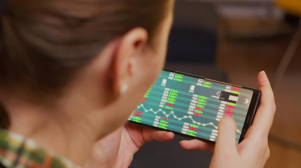 Over-the-shoulder view of a woman checking stock market data on her phone