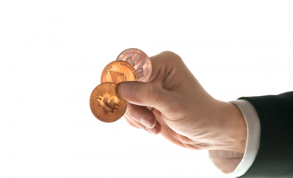 hand holds three cryptocurrency coins on a white background