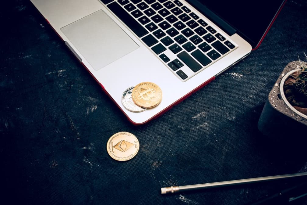 three coins, an opened laptop, and a small vase with a cactus on the black table